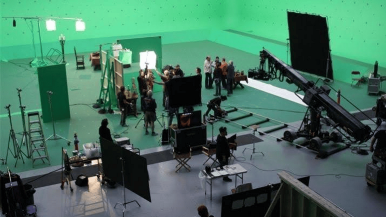 A film crew works in a large green-screen studio with lights, cameras, and a crane.